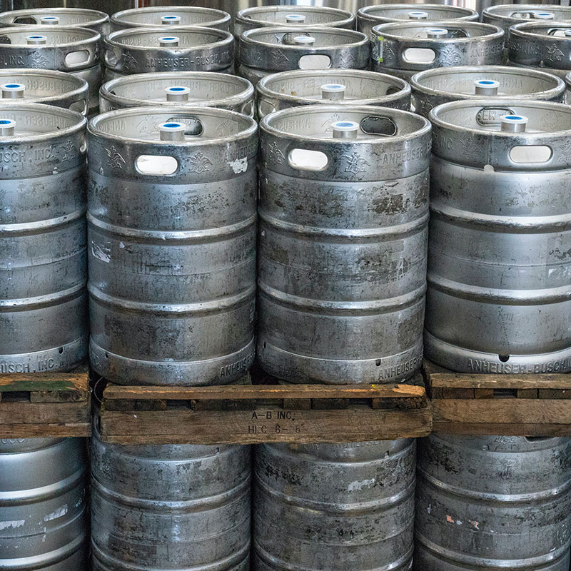 Multiple gray kegs stacked and separated by a wooden board.