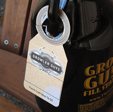 Paper tag that reads "Growler Guys" attached to a glass bottle.
