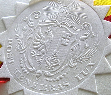 An engraved white paper in the form of the sun showing a banner.