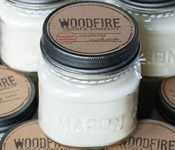 Transparent jar with a metallic lid that reads "Woodfire Candle Company".