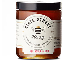 A jar of honey with a white label that reads "State Street Honey" and a black lid.
