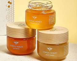 Three containers of honey with wooden lid and transparent labels.