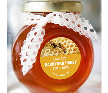 Small jar of honey with metal lid and white ribbon and a yellow label.