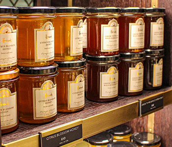 A shelf stacked with jars of honey with white labels.