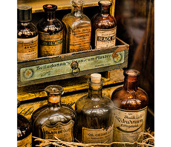 Old apothecary glass bottles on shelves with vintage labels.