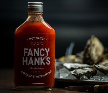 A glass bottle of sauce that reads "Fancy Hank's" with a metal lid.
