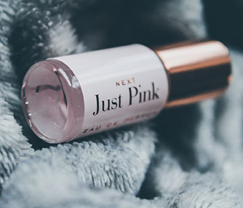 A pink container that reads "Just Pink" with a golden lid on a blanket.